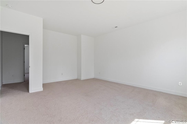 spare room featuring light carpet and baseboards