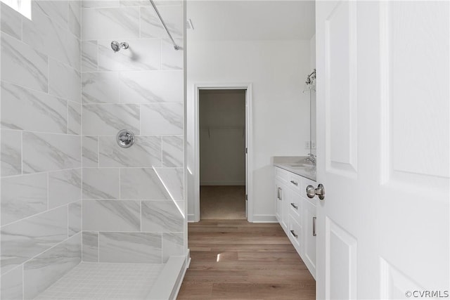 full bathroom with a walk in closet, wood finished floors, baseboards, tiled shower, and vanity