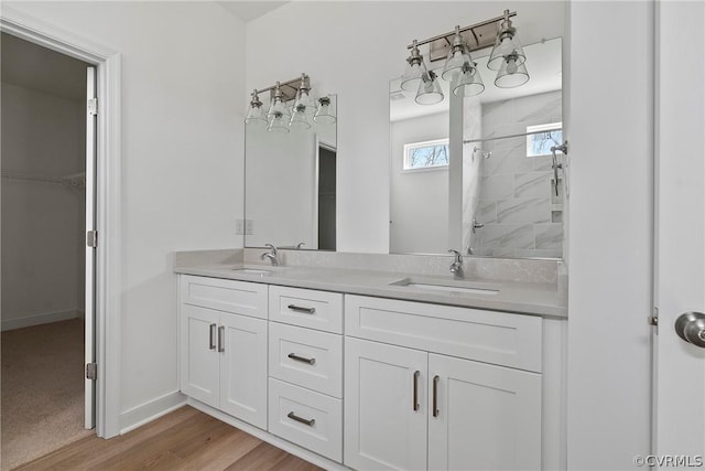 full bath featuring a sink, wood finished floors, a tile shower, double vanity, and a spacious closet