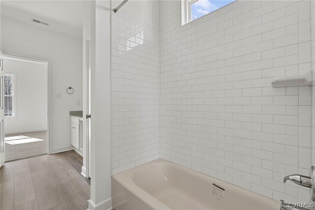 bathroom with wood-type flooring, tiled shower / bath, and vanity