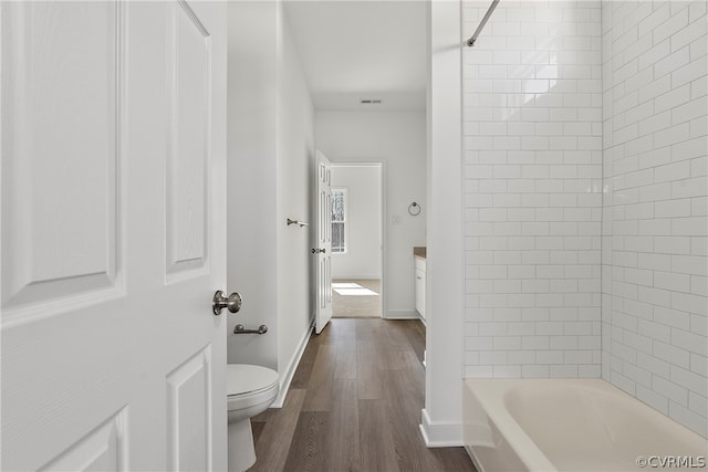 full bathroom with wood-type flooring, tiled shower / bath, vanity, and toilet