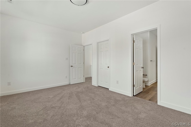 unfurnished bedroom with ensuite bathroom and dark colored carpet