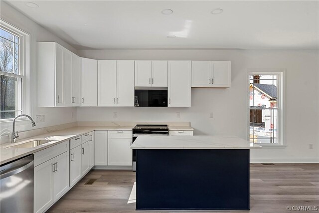 kitchen with a center island, white cabinetry, light wood-type flooring, appliances with stainless steel finishes, and sink