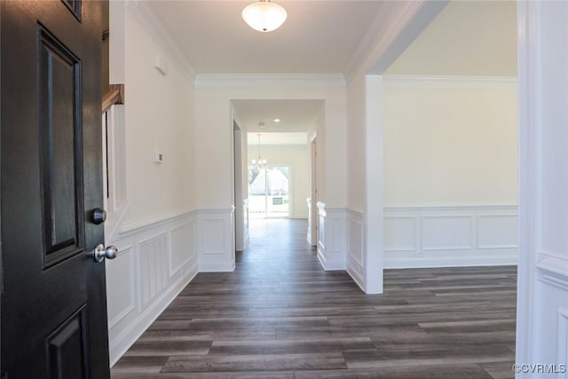 hall with crown molding, dark wood-type flooring, a decorative wall, and a notable chandelier