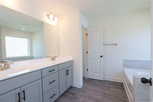 bathroom featuring hardwood / wood-style floors, tiled bath, and double sink vanity