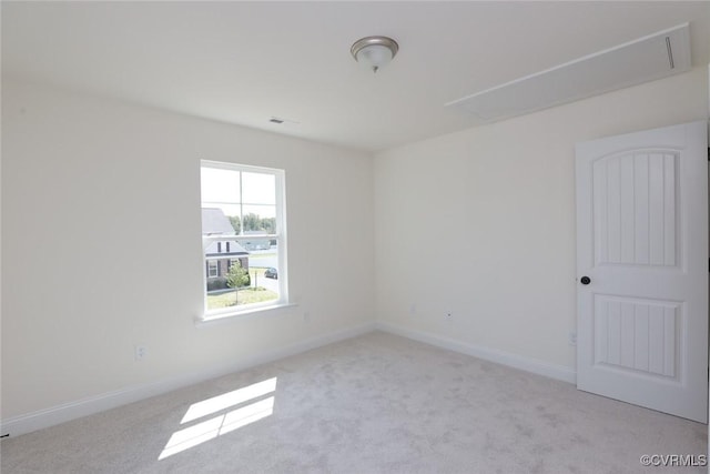 carpeted empty room featuring attic access and baseboards