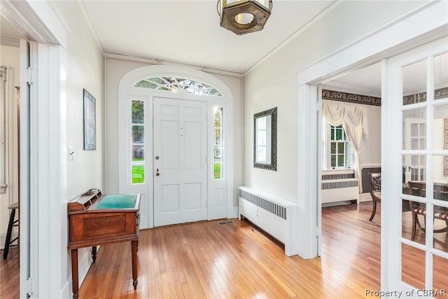 entrance foyer featuring radiator heating unit, ornamental molding, and light hardwood / wood-style flooring