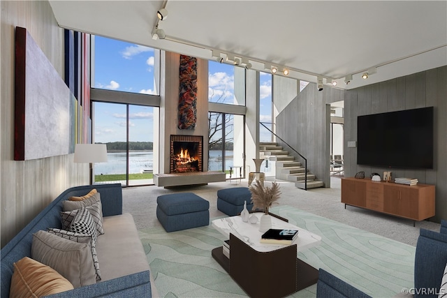 living room featuring expansive windows, a fireplace, a water view, rail lighting, and light colored carpet