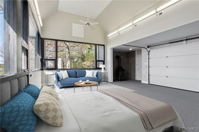 carpeted bedroom featuring high vaulted ceiling, a wood stove, and ceiling fan