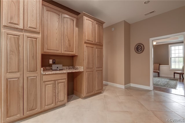 kitchen with light brown cabinetry, light stone countertops, and light tile patterned floors