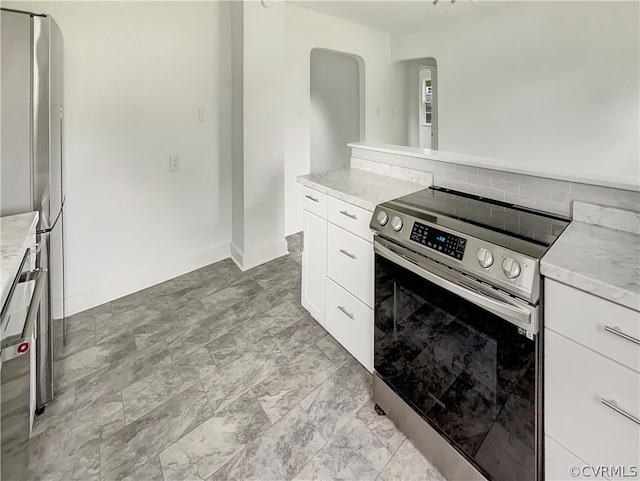 kitchen featuring appliances with stainless steel finishes, light tile floors, tasteful backsplash, white cabinetry, and light stone countertops