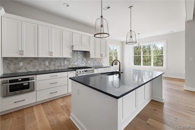 kitchen featuring an island with sink, stainless steel appliances, tasteful backsplash, and light wood-type flooring