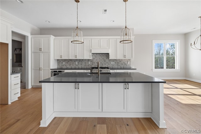 kitchen with backsplash, a center island with sink, light hardwood / wood-style floors, and decorative light fixtures