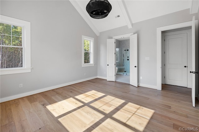 unfurnished bedroom with beamed ceiling, high vaulted ceiling, connected bathroom, and light wood-type flooring