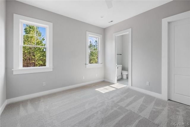 unfurnished bedroom with ceiling fan, multiple windows, light colored carpet, and ensuite bath