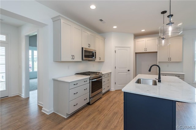 kitchen featuring a center island with sink, stainless steel appliances, pendant lighting, light hardwood / wood-style flooring, and sink