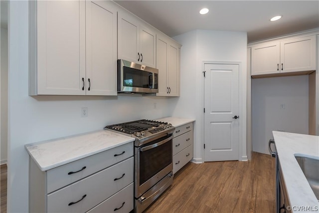 kitchen featuring light stone countertops, light wood-type flooring, appliances with stainless steel finishes, and white cabinetry