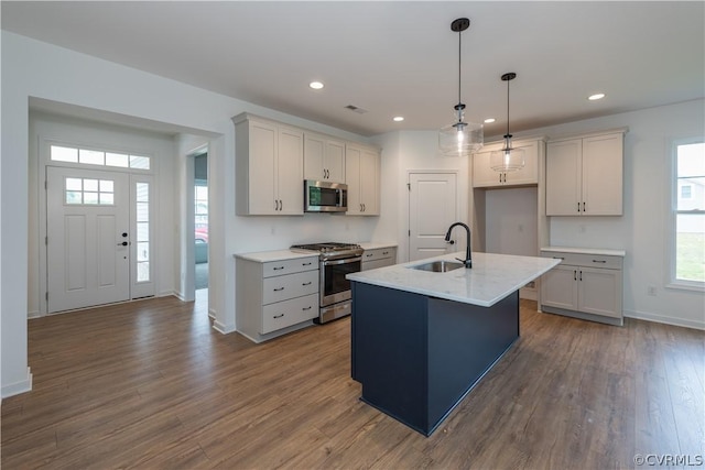 kitchen with pendant lighting, wood-type flooring, stainless steel appliances, sink, and a center island with sink