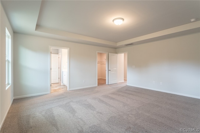 unfurnished bedroom with a closet, light colored carpet, a raised ceiling, and a walk in closet