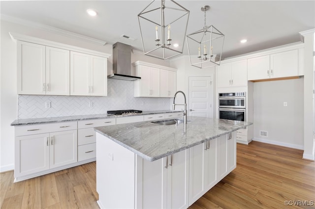 kitchen featuring wall chimney exhaust hood, white cabinets, and a center island with sink