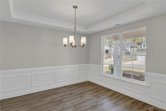 unfurnished dining area featuring a notable chandelier, wood-type flooring, a tray ceiling, and crown molding