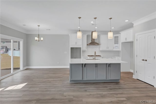 kitchen with wall chimney exhaust hood, white cabinetry, decorative light fixtures, and a center island with sink