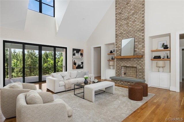 living room with brick wall, a fireplace, light wood-type flooring, built in shelves, and high vaulted ceiling