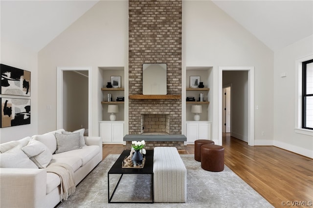 living room with high vaulted ceiling, built in features, hardwood / wood-style flooring, and a fireplace