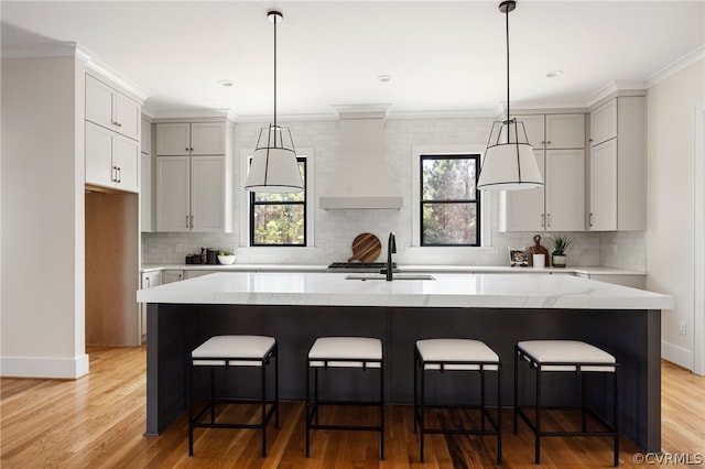 kitchen featuring sink, an island with sink, custom range hood, and light hardwood / wood-style flooring