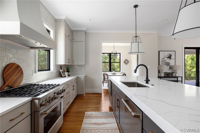 kitchen featuring wall chimney range hood, appliances with stainless steel finishes, hardwood / wood-style flooring, decorative light fixtures, and backsplash