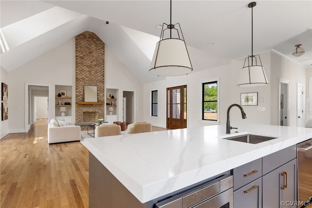 kitchen featuring brick wall, a fireplace, a kitchen island with sink, light wood-type flooring, and sink