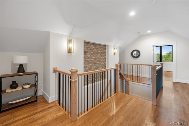 hallway with brick wall, lofted ceiling, and wood-type flooring