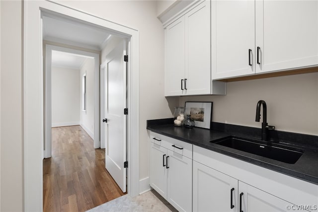 kitchen with sink, hardwood / wood-style flooring, white cabinetry, and crown molding