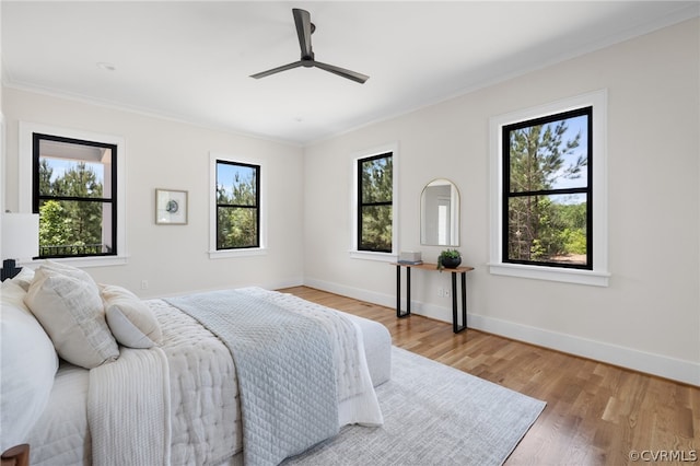 bedroom featuring ceiling fan, multiple windows, light wood-type flooring, and ornamental molding