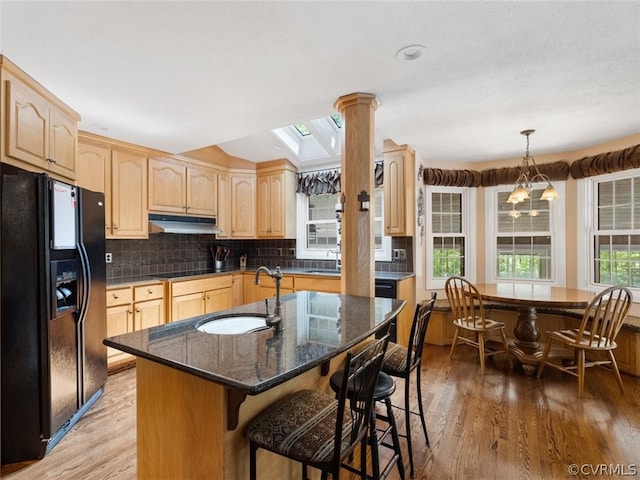 kitchen featuring light hardwood / wood-style flooring, tasteful backsplash, a center island with sink, pendant lighting, and black appliances