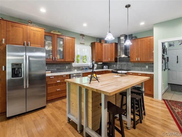 kitchen featuring a center island, wall chimney range hood, hanging light fixtures, light hardwood / wood-style flooring, and stainless steel refrigerator with ice dispenser