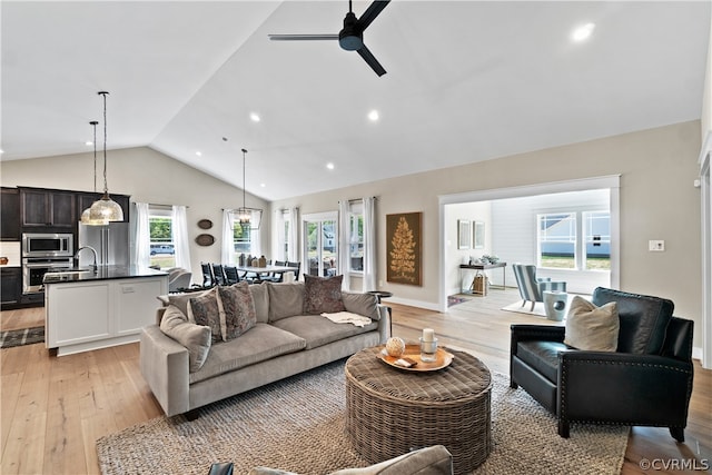 living room with a wealth of natural light, high vaulted ceiling, ceiling fan, and light wood-type flooring