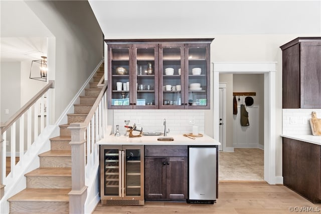 bar with wine cooler, light hardwood / wood-style floors, tasteful backsplash, dark brown cabinetry, and sink