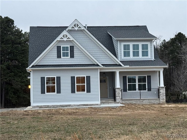 craftsman inspired home featuring roof with shingles, a porch, and a front yard