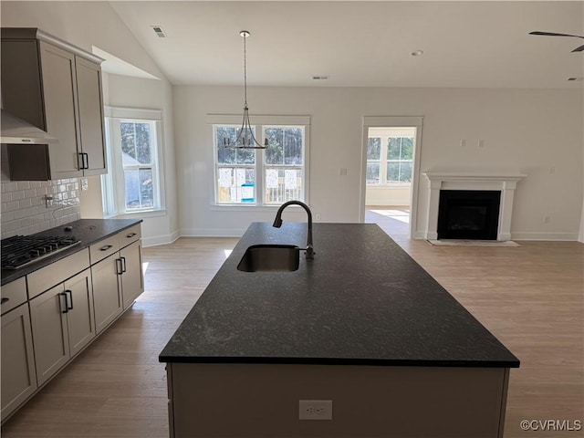 kitchen featuring stainless steel gas stovetop, decorative backsplash, a sink, an island with sink, and light wood-type flooring