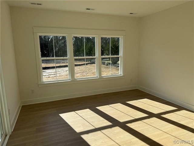 empty room featuring dark wood-style flooring, visible vents, and baseboards