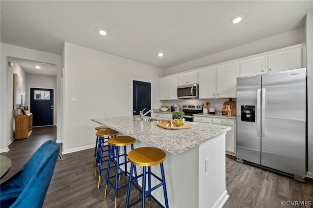 kitchen with white cabinets, dark hardwood / wood-style floors, stainless steel appliances, and an island with sink