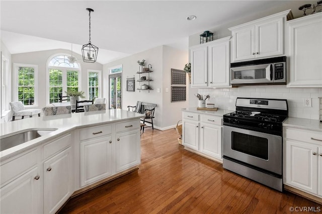 kitchen with lofted ceiling, stainless steel appliances, tasteful backsplash, white cabinets, and decorative light fixtures