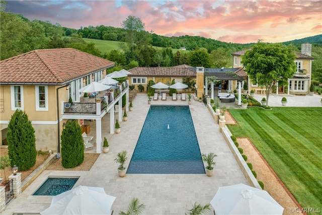 pool at dusk with a patio area, a pergola, and a lawn