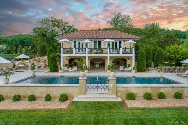 pool at dusk featuring a patio and a lawn