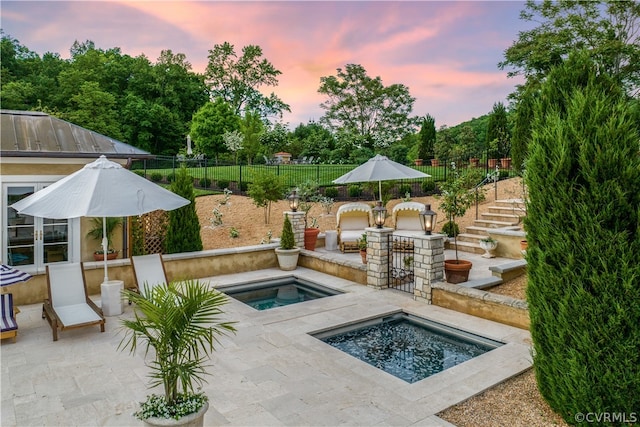 pool at dusk featuring a patio and an in ground hot tub