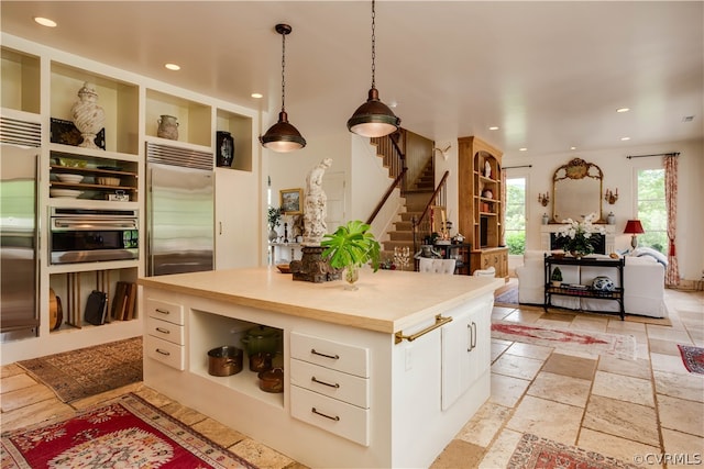 kitchen with stainless steel appliances, pendant lighting, a kitchen island, light tile floors, and white cabinetry