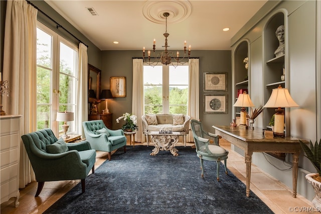 sitting room with a healthy amount of sunlight, tile flooring, built in shelves, and a notable chandelier