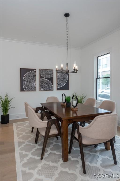 dining area with baseboards, a notable chandelier, light wood-style flooring, and crown molding