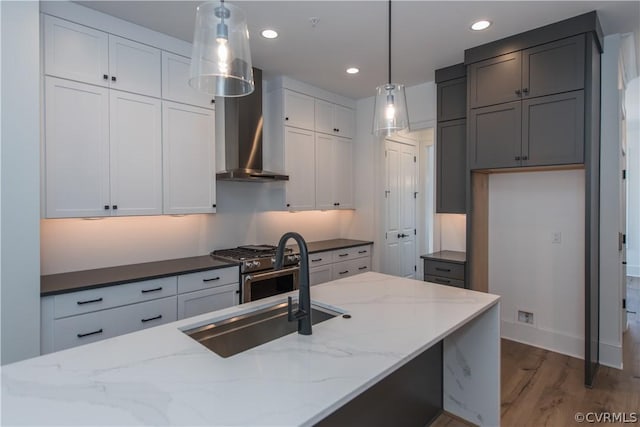 kitchen with hanging light fixtures, dark stone counters, light wood-style flooring, and wall chimney exhaust hood